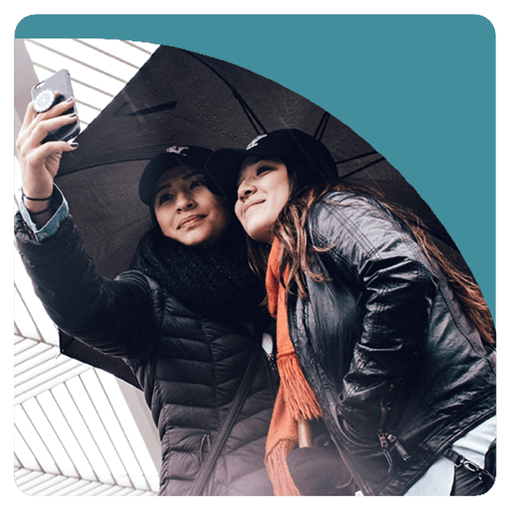 Two young adult women taking a selfie under an umbrella